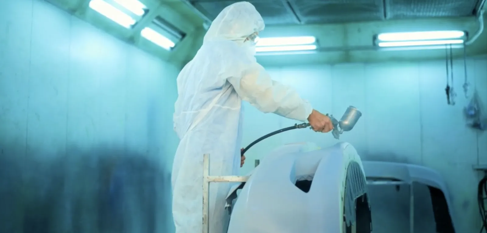 Technician applying a spray coating inside a controlled paint booth